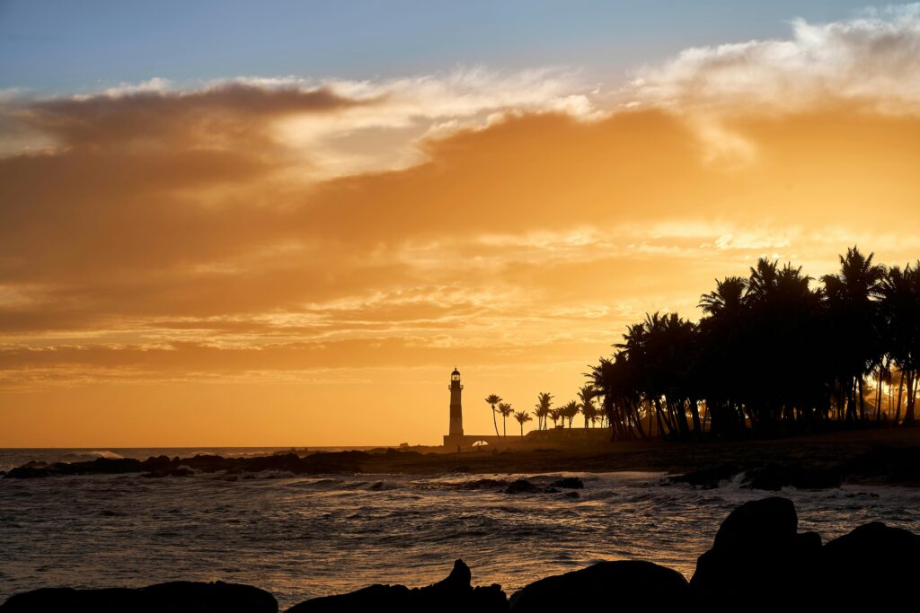 Stunning sunset with a lighthouse silhouette and palm trees in Salvador, Brazil.